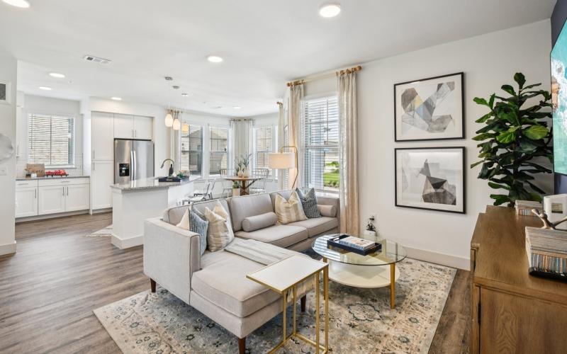 a living room with a couch and a table leading into a kitchen with windows