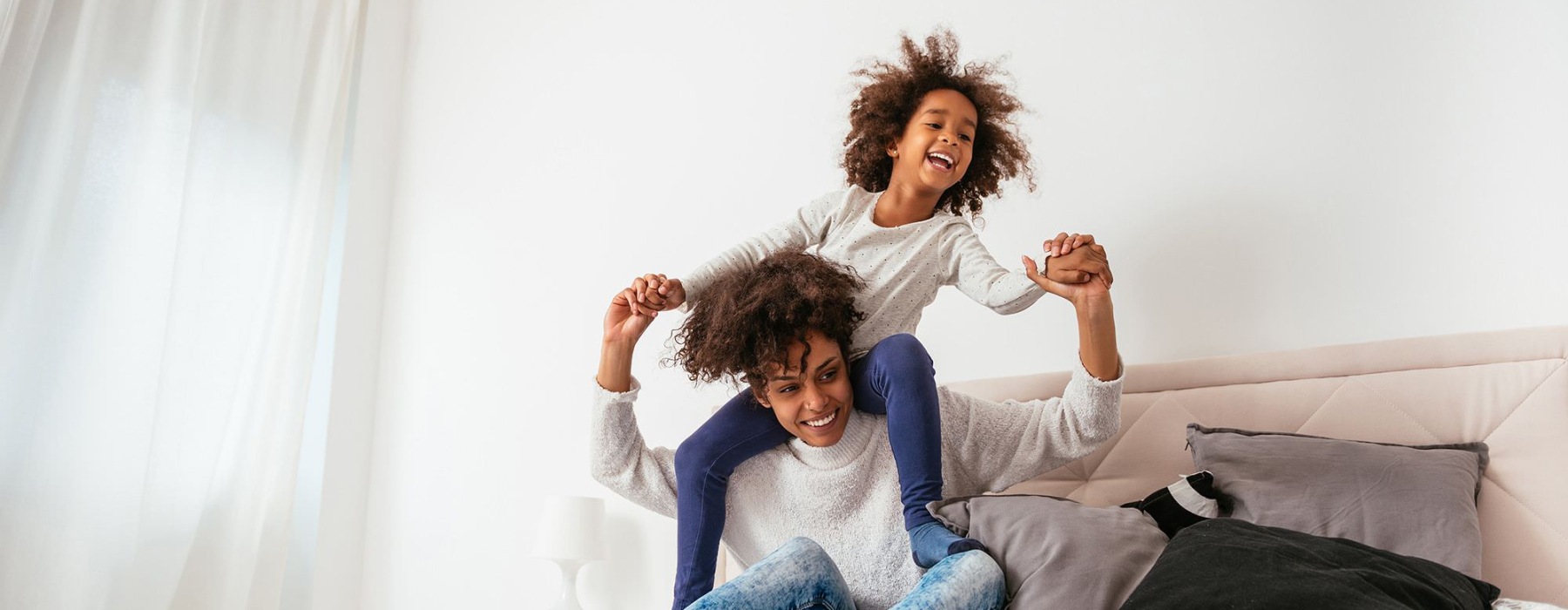 mother and daughter happily play on a large bed